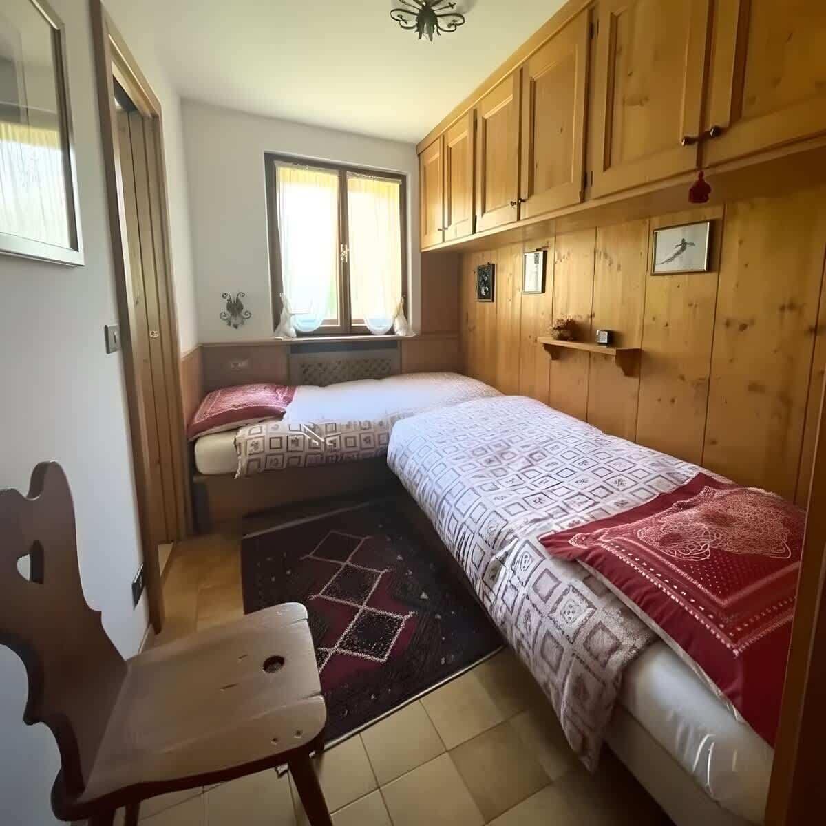 A small room with two beds, wooden cabinets, a window, and a chair.