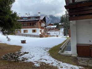 A snow-covered landscape with a wooden building featuring a balcony and a stone pathway leading to it. - Casa Verocai Classic Retreat in Cortina (Cortina d'Ampezzo)