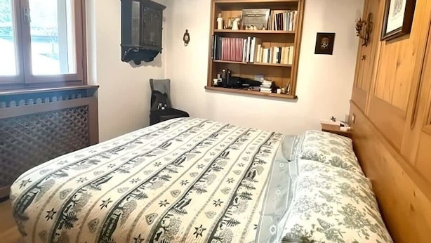 A bedroom with a bed, a bookshelf, a chair, and a window. - Casa Verocai Classic Retreat in Cortina (Cortina d'Ampezzo)