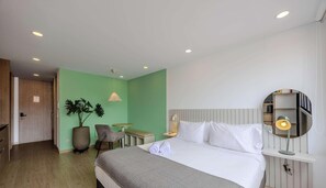 Et hotelværelse med seng, sengebord, lampe, en potteplante, stol og et spejl.
