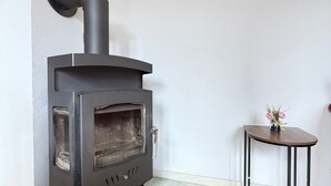 A modern wood stove with a black chimney, a small table with a vase of flowers, and a wooden floor. - Oberburg | Unique vacation apartment in a historic castle. (Kobern)