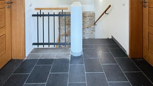 A hallway with a black-tiled floor, wooden doors, a white pillar, and a stone wall. - Oberburg | Unique vacation apartment in a historic castle. (Kobern)