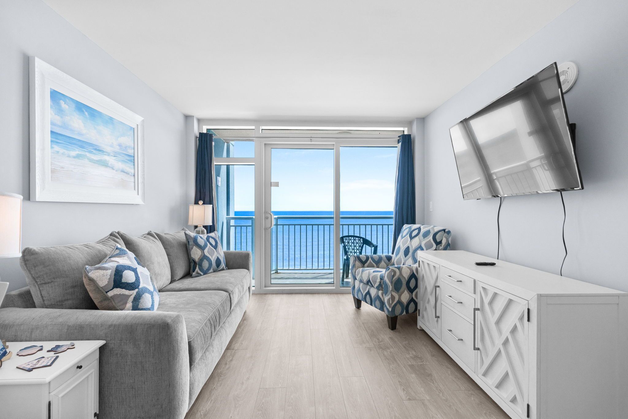 A modern room with a sofa, armchair, TV, and a balcony with a view.