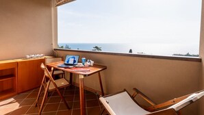Un balcón con un escritorio de madera, una computadora portátil y vista al mar.