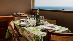 Mesa de comedor dispuesta con platos, vasos y una botella de champán, con vistas al mar.