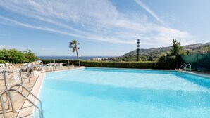 Piscina con vista al mar, rodeada de sillones de descanso y un seto.