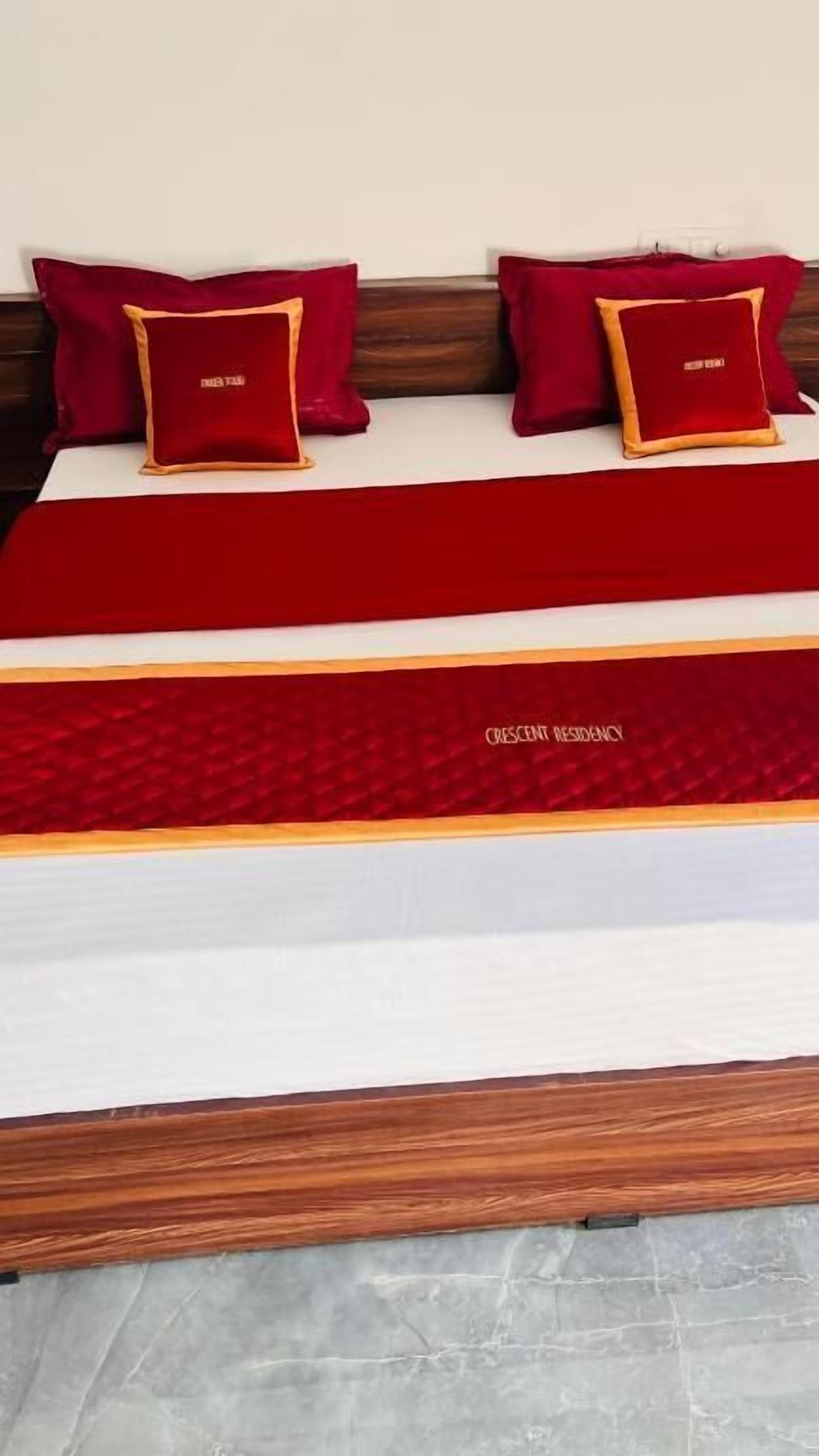 A bed with a red and white bedspread, two red pillows with gold trim, and a wooden headboard.