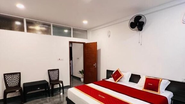 A hotel room with a large bed, a desk, two chairs, a fan, and a door. - Crescent Residency Wayanad (Vythiri)
