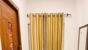A bathroom with a wooden door, a sink, a toilet, a shower curtain, and a small table with a tray. - Crescent Residency Wayanad (Vythiri)
