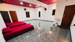 A hotel room with a marble floor, two red beds, a wooden door, and a white sink. - Crescent Residency Wayanad (Vythiri)