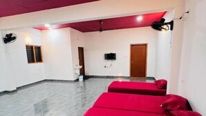 A room with two red beds, a white sink, a wooden door, and a television on the wall. - Crescent Residency Wayanad (Vythiri)