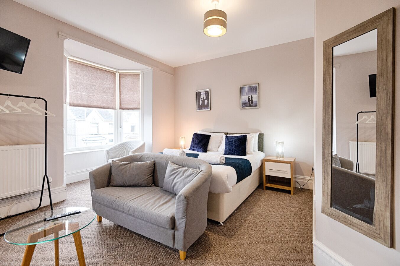 A modern bedroom with a bed, a sofa, a bedside table, a TV, and a large mirror.