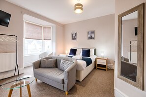 A modern bedroom with a bed, a sofa, a bedside table, a TV, and a large mirror. - Double Room with Kitchen & Parking | Gorseinon Swansea (Gorseinon)