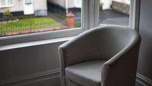 Ein Stuhl am Fenster mit Blick auf einen Garten und Gebäude.