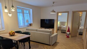 A modern living room with a sofa, TV, dining table, and chairs. - Willa Marianna - apartamenty wakacyjne (Lądek-Zdrój)
