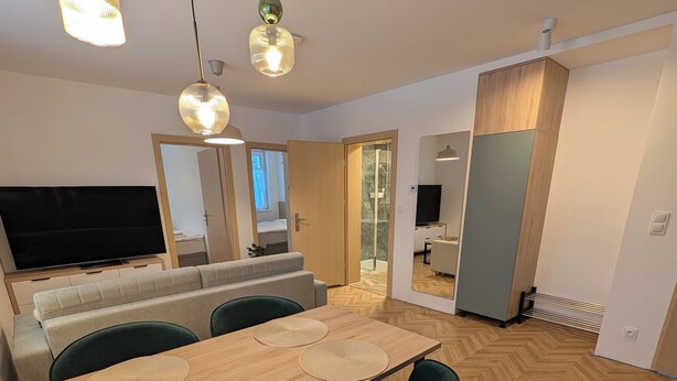 A modern living room with a wooden dining table, green chairs, a sofa, and a TV. - Willa Marianna - apartamenty wakacyjne (Lądek-Zdrój)