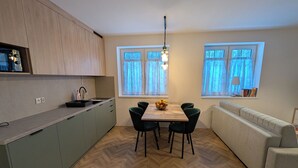 A compact kitchen with a dining table and chairs, a sofa, and a window with curtains. - Willa Marianna - apartamenty wakacyjne (Lądek-Zdrój)