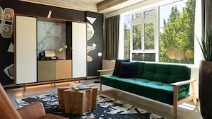A modern living room with a green sofa, a wooden coffee table, and a large window with a view of trees.