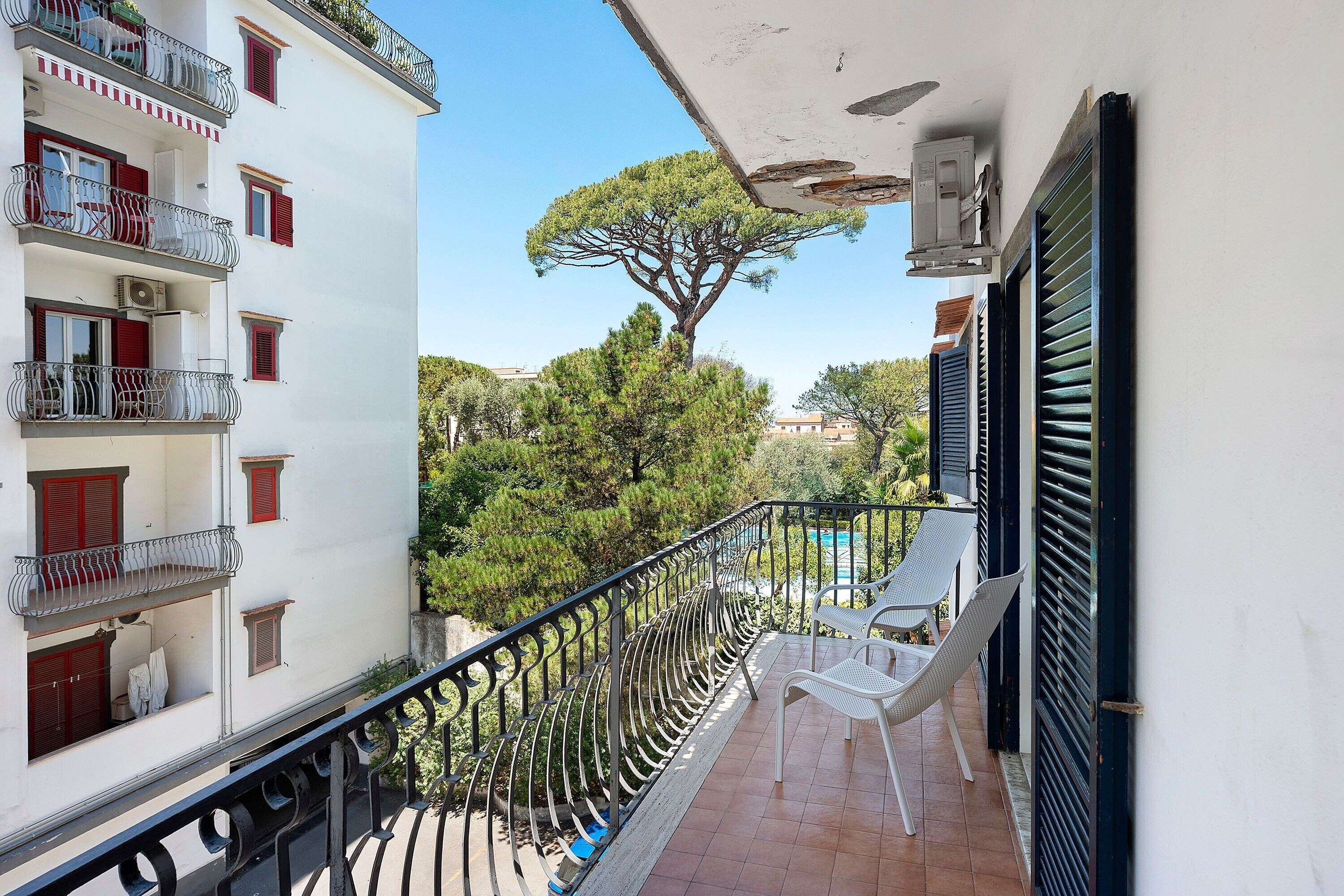 A balcony with a metal railing, a white chair, and a view of trees and buildings.