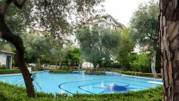 A swimming pool surrounded by trees and bushes, with a building in the background.