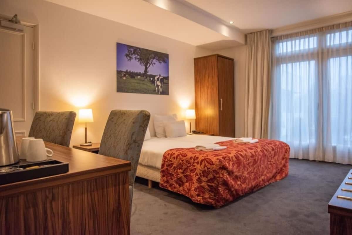 Ein Hotelzimmer mit einem Bett, zwei Stühlen, einem Schreibtisch mit Kaffeemaschine, einem Schrank und einem Bild an der Wand.