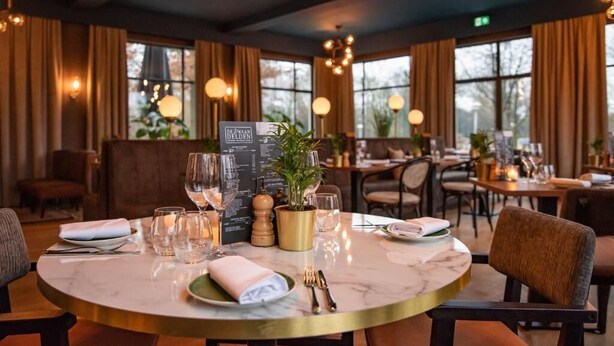 A restaurant with round tables, candles, and a menu stand. - De Zwaan Delden (Delden)
