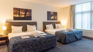 A hotel room with two beds, a large window with curtains, and artwork on the walls. - De Zwaan Delden (Delden)