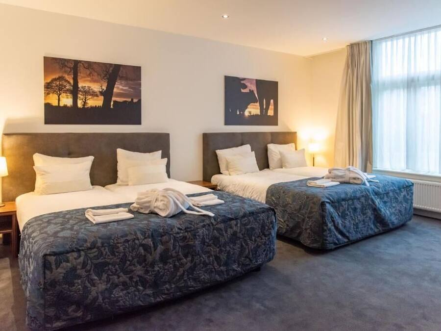 Habitació d'hotel amb dos llits, una finestra gran amb cortines i obres d'art a les parets.