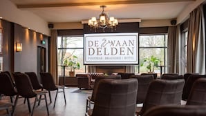 A conference room with rows of chairs, a chandelier, and a sign for 'De Zwaan Delden' foodbar, brasserie, and hotel. - De Zwaan Delden (Delden)