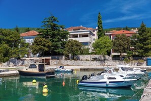 Eine Marina mit vertäuten Booten, eine Steinmauer und Gebäude mit roten Dächern im Hintergrund.