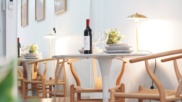 Un intérieur moderne avec des chaises et des tables en bois, une bouteille de vin et une plante en pot posée sur une table.