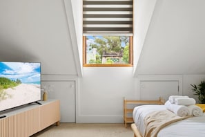 Un dormitorio con televisión, cama, ventana con vistas y techo inclinado.