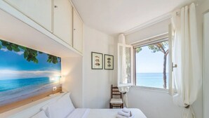Habitación de hotel con cama, ventana con cortinas, una silla y un muro con cuadros.