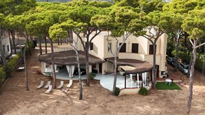 Una villa con zona de estar exterior cubierta, piscina y jardín ajardinado con árboles.