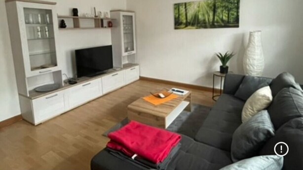 Ein modernes Wohnzimmer mit Flachbildfernseher, einer Couch, einem Couchtisch und einem Bücherregal.