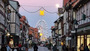Eine Straße gesäumt von traditionellen Gebäuden, einem Riesenrad und festlicher Weihnachtsbeleuchtung.