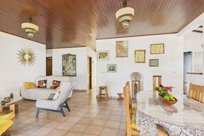 A spacious living room with a dining area, wooden ceiling, and various wall art. - House near the sea with garden 6 guests (La Trinité)