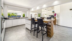 Una cocina moderna con armarios blancos, una isla central con taburetes y vistas a zonas verdes.