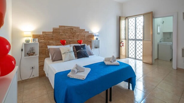 A hotel room with a bed, bedside tables, a nightstand, a blue bedspread, heart-shaped balloons, and a wooden headboard. - Brezza Salentina House Giardino Privato (Porto Cesareo)