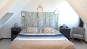 A bedroom with a sloped ceiling, a bed with striped bedding, two bedside tables with decorative items, and a chair. - Duplex sea view - Terrace - Near the sea - Rated 3*. (Trébeurden)
