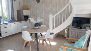 A modern kitchen with white cabinets, a dining table with chairs, a TV, and a staircase. - Duplex sea view - Terrace - Near the sea - Rated 3*. (Trébeurden)