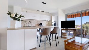 Eine moderne Küche mit weißen Schränken, einer zentralen Kochinsel, Barhocker, einem Fernseher und einem Balkon mit Blick.