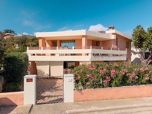 A two-story building with a balcony, a gated entrance, and a well-maintained garden with pink flowers. - Arvella Stay I by Klodge – Beachfront Suite (Olbia)