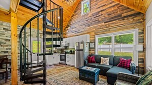 A cabin interior with a spiral staircase, a kitchenette, a sofa with decorative pillows, and a large window.