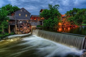 Een watermolen met een houten rad, een houten huis met veranda en een vijver.