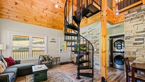 A cozy living room with a spiral staircase, a fireplace, and a stone wall.