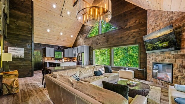 A spacious living area with a large sofa, a fireplace, and a kitchen in the background. - New! 5BR cabin w/Hot Tub*Theater*Arcade*Fireplace (Pigeon Forge)