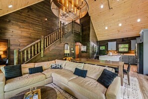Ein Blockhaus-Interieur mit einer Holztreppe, einem Ecksofa, einer Küchenzeile und einem Esstisch.