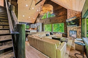 Ein modernes Interieur mit einer Holztreppe, einer gemütlichen Sitzecke, einer Küche und großen Fenstern mit Blick ins Freie.