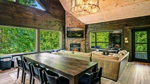 A spacious living area with a large wooden table, seating, a fireplace, and a stone wall. - New! 5BR cabin w/Hot Tub*Theater*Arcade*Fireplace (Pigeon Forge)